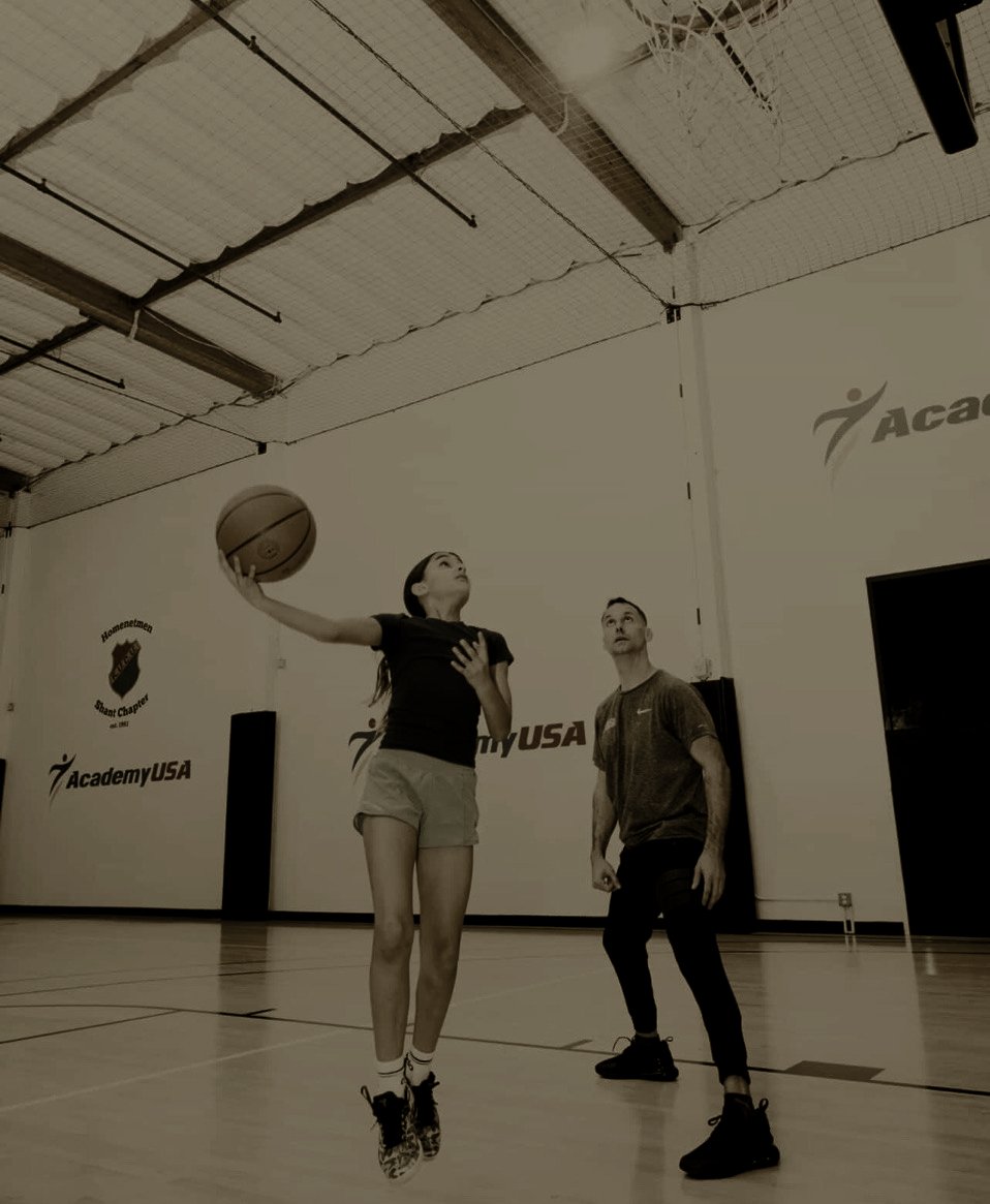 Coach Shaun Gerardo watches a young athlete finish a layup during training